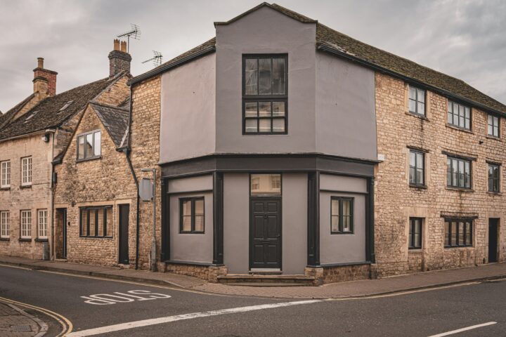 Corner heritage building with stone facade, grey painted section, and dark windows.