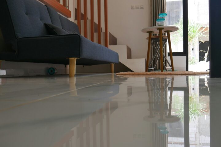 Glossy epoxy flooring reflecting a modern living room with a sofa and stairs.