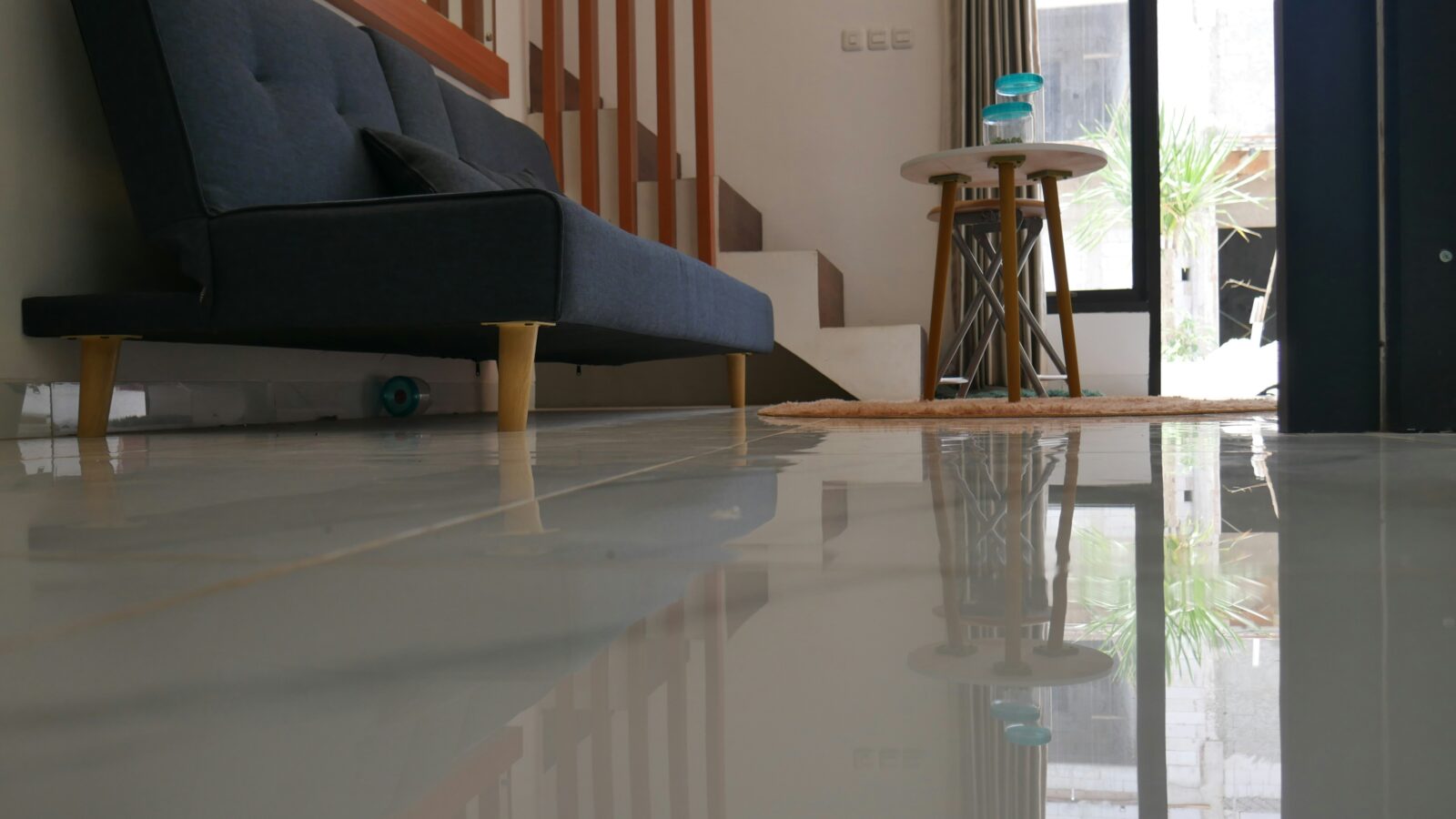 Glossy epoxy flooring reflecting a modern living room with a sofa and stairs.